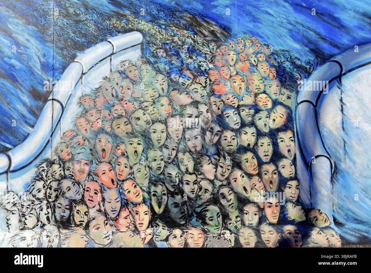 Eine Vielzahl surrealer gemalter Gesichter drängen sich zusammen, umgeben von blauen und hellen Farben, Graffiti an der Berliner Mauer in der East Side Gallery, Berl Stockfoto
