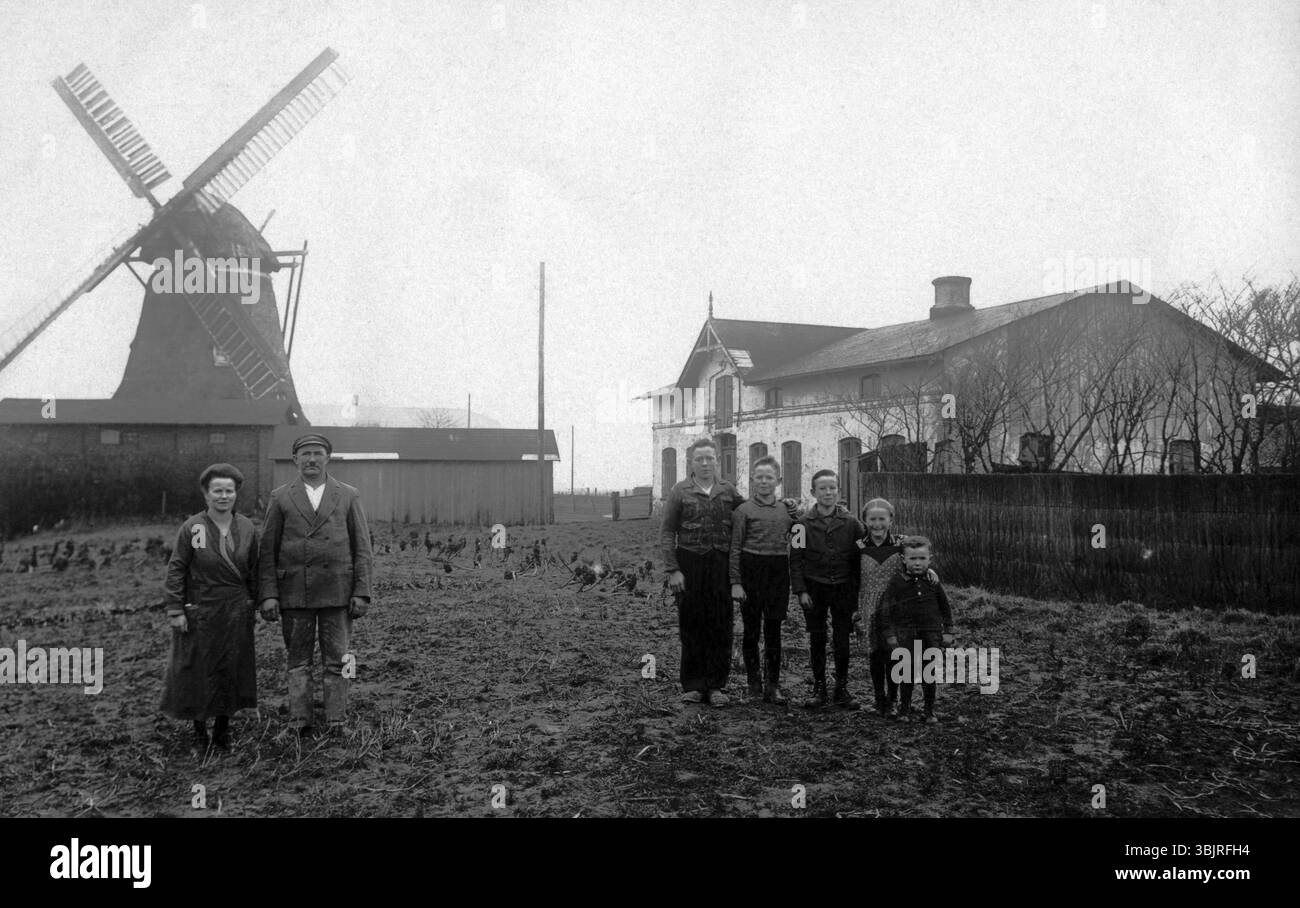 Bauernfamilie auf einem Feld mit einer Windmühle im Hintergrund, 1930er Jahre, Familie auf einem Bauernhof in der Nähe eines Feldes mit einer Windmühle im Hintergrund in einem rura Stockfoto