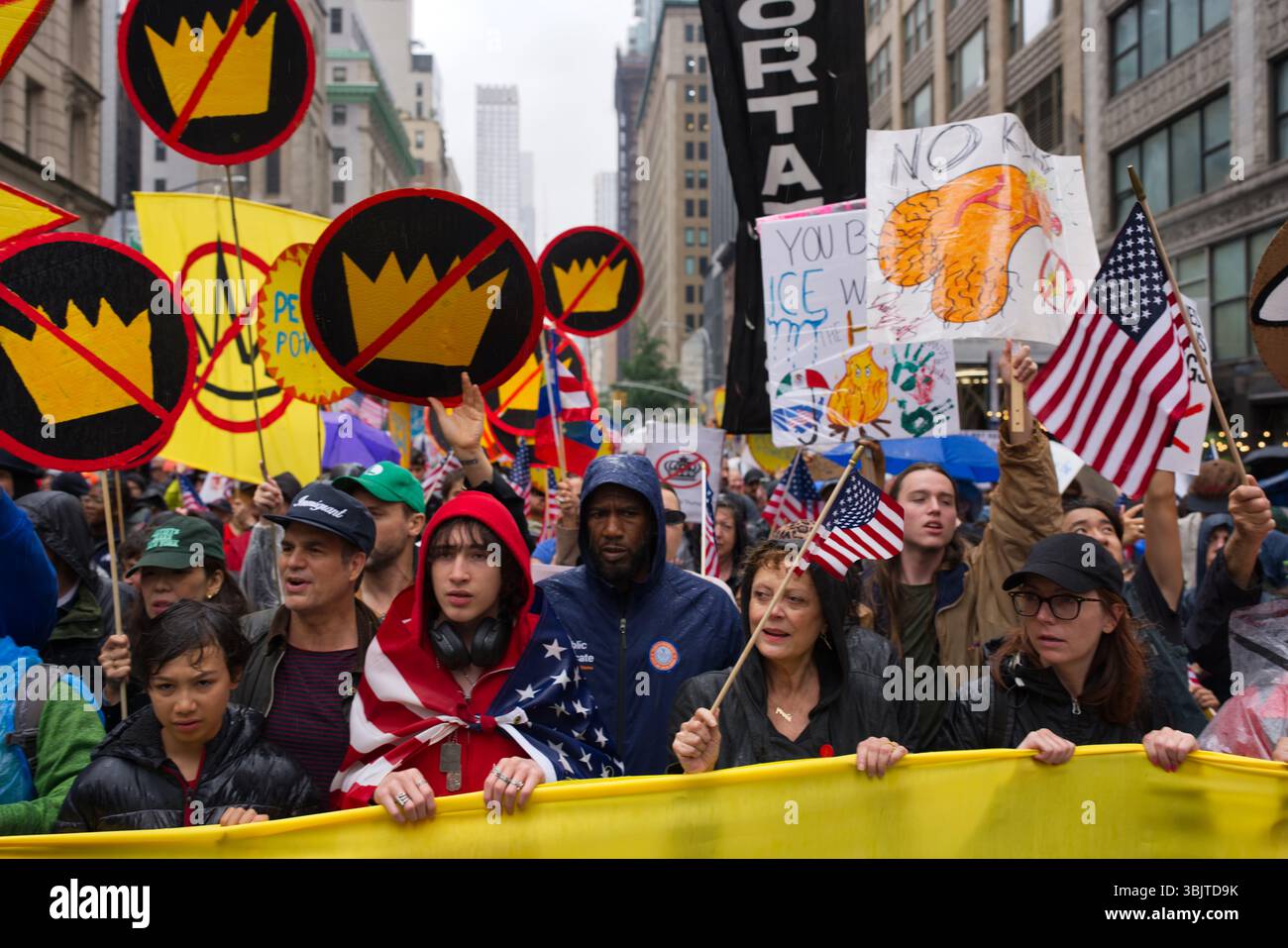 Eine große Gruppe von Demonstranten marschiert eine Stadtstraße hinunter und hält Schilder mit verschiedenen Botschaften und Symbolen, darunter Kronen mit Schlitzen durch sie und Stockfoto