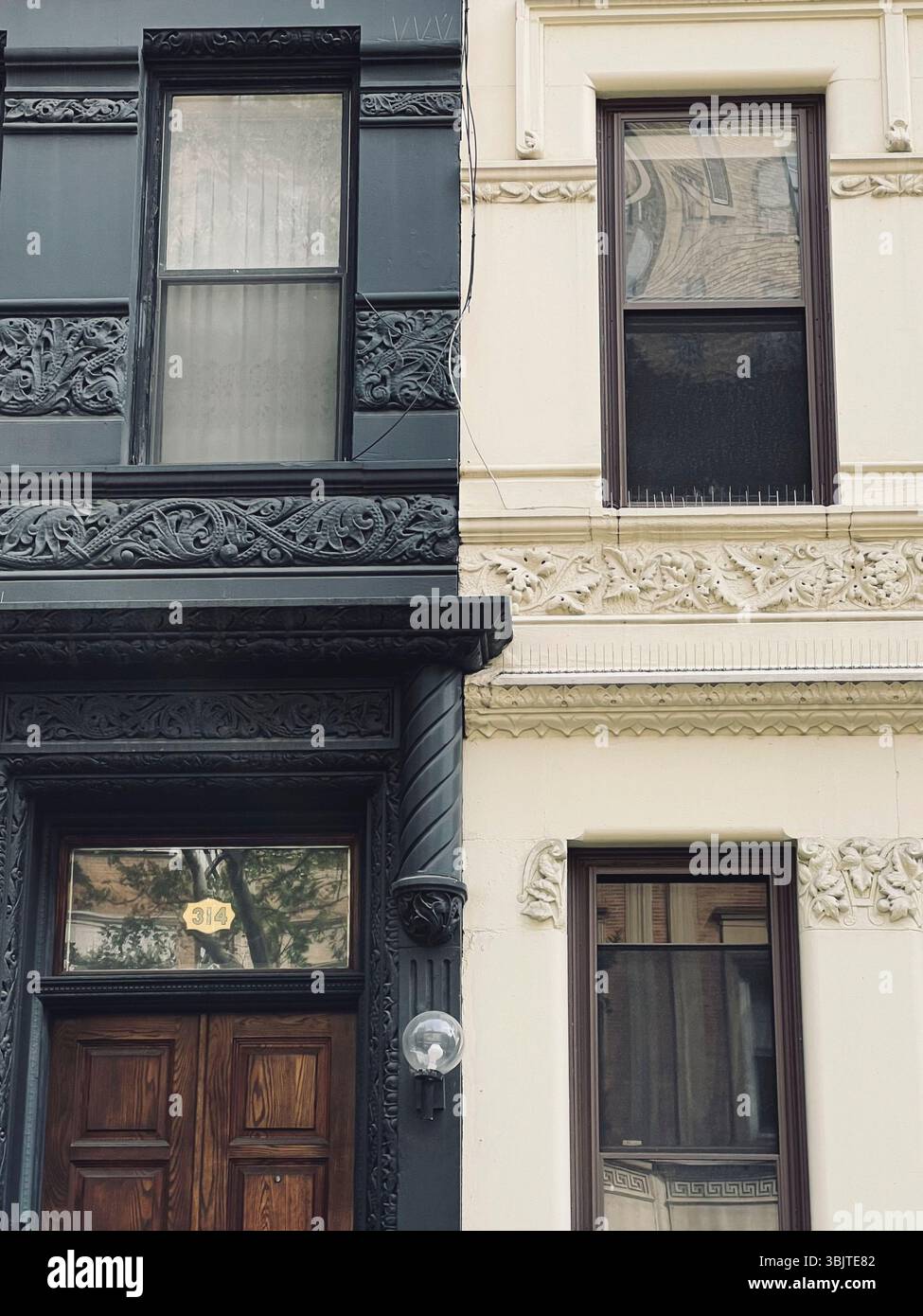 Eine Nahansicht eines Gebäudes im Brownstone-Stil in New York City, die einen Kontrast zwischen zwei angrenzenden Fassaden zeigt – eine schwarz und die andere weiß. - Smartphone-aufgenommenes Stockfoto