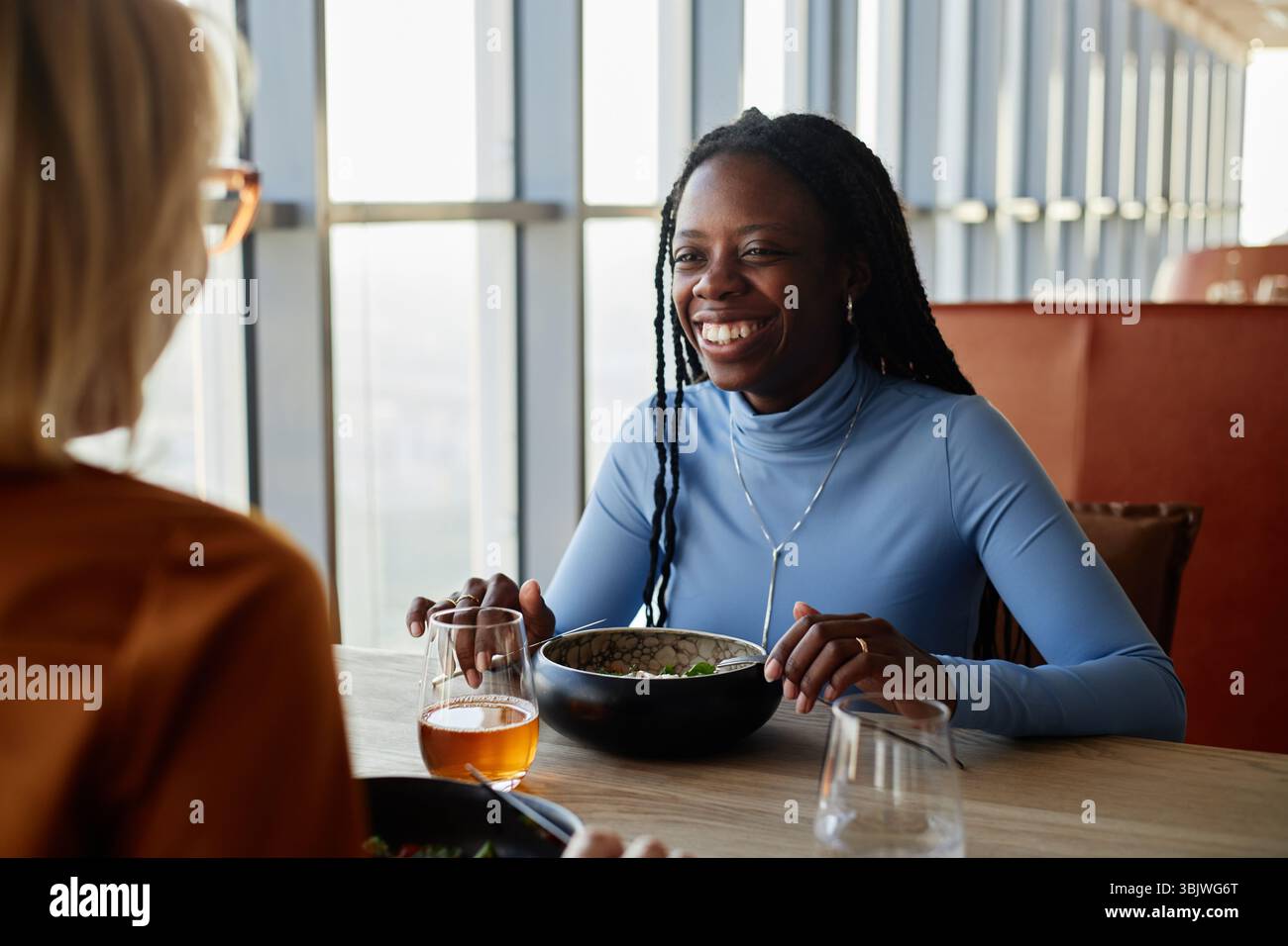 Junge Erwachsene Schwarze Frau lächelt beim Mittagessen mit einer Kaukasierin Stockfoto