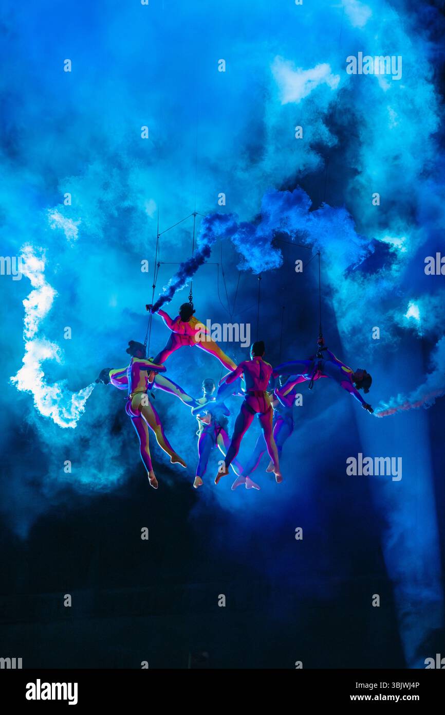 Luftdarsteller von NEXUS von Sylphes Aerial Ballet und Collectif Arbuste schwebten in der Luft und setzten leuchtend blauen Rauch am Nachthimmel ab Stockfoto
