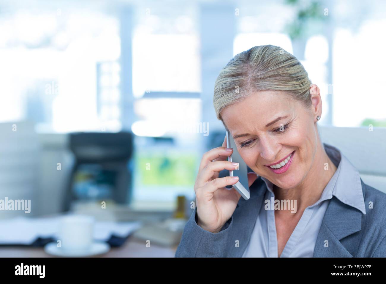 Smartphone auf Schreibtisch mit weißer Kaffeetasse und verstreuten Papieren in der Nähe von Fenstern Stockfoto
