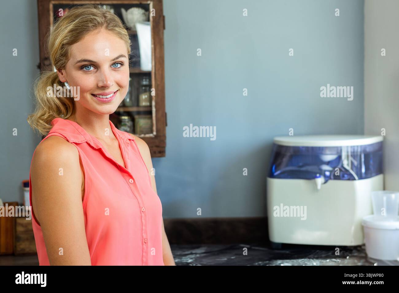 Wasserreiniger auf der Arbeitsplatte unter der hellblauen Wand mit Holzschrank mit Glasgläsern Stockfoto