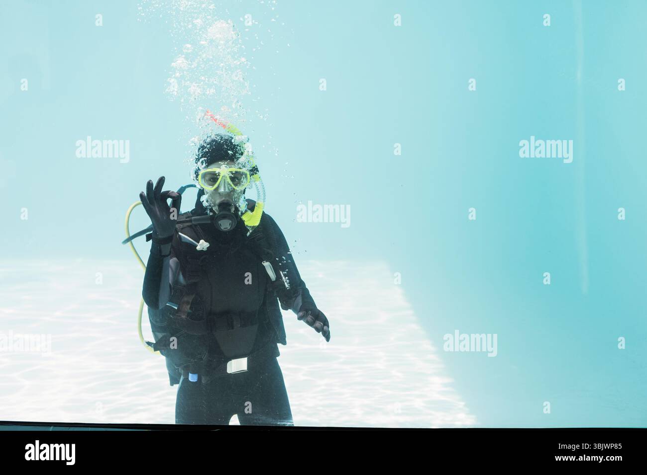 Taucher mit gelber Tauchermaske und Tauchbecken, die im klaren Poolwasser schweben, Blasen steigen auf Stockfoto