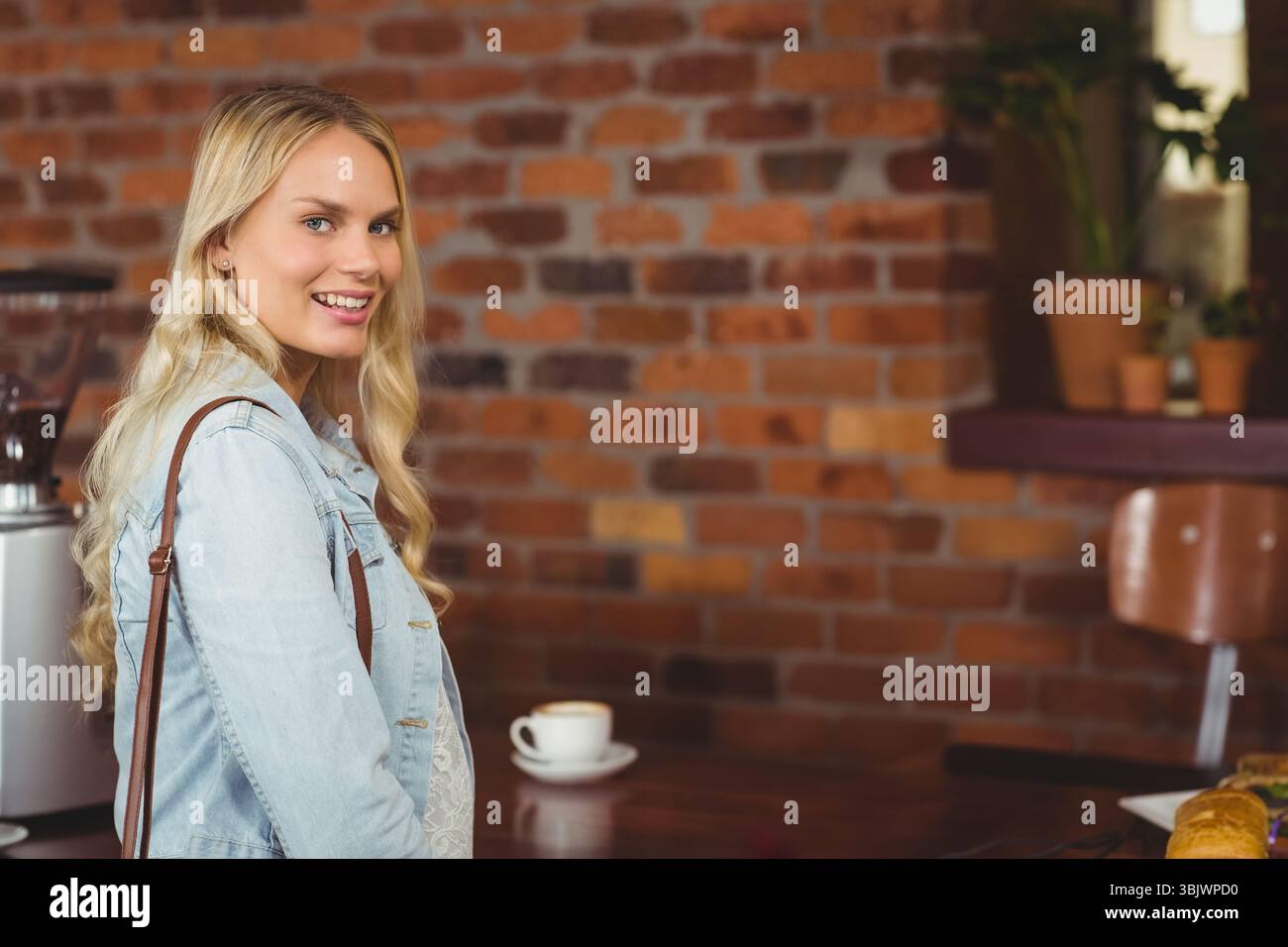 Weiße Kaffeetasse auf Holztisch mit Gebäck neben roter Ziegelwand und Topfpflanzen Stockfoto