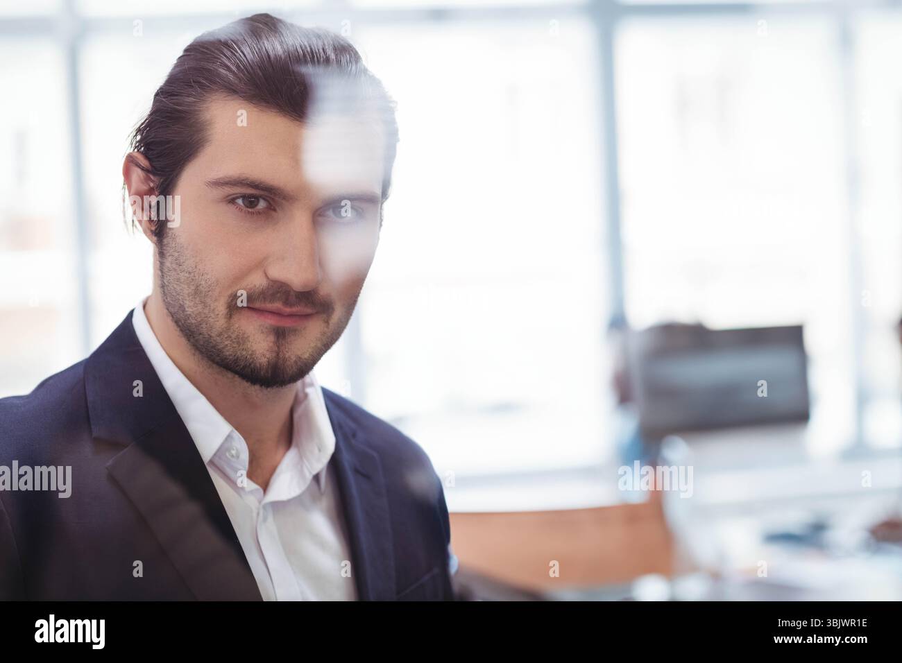 Mann, der hinter einer Glaswand am modernen Schreibtisch steht, Computermonitor und Kopierraum ansieht Stockfoto