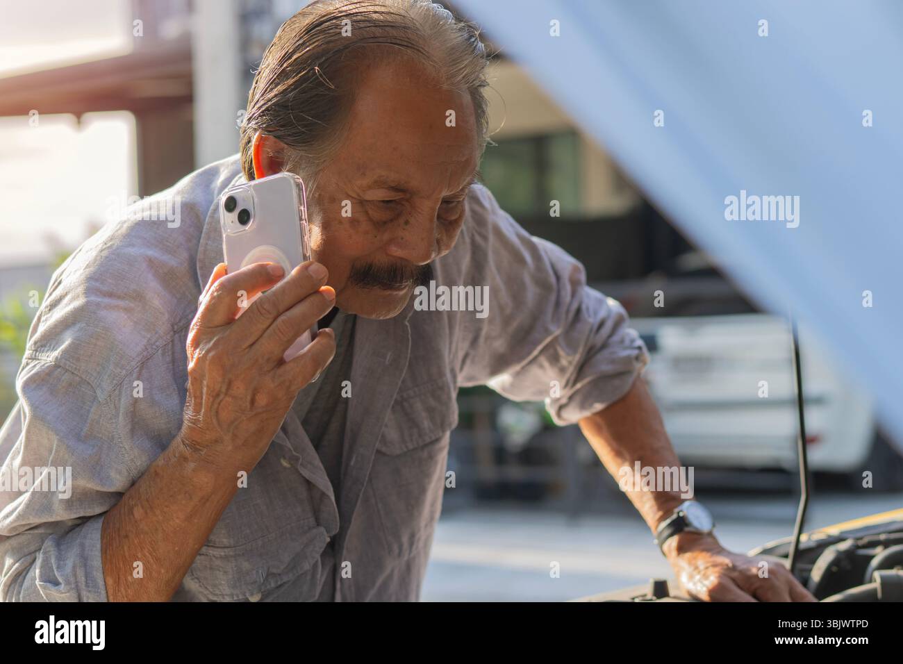 Ein reifer Mann, der versucht, sein Auto zu reparieren, wenn er mit einem Mechaniker telefoniert. Ein Autobesitzer ruft eine Autowerkstatt an, um den Zustand des Autos zu überprüfen. Stockfoto