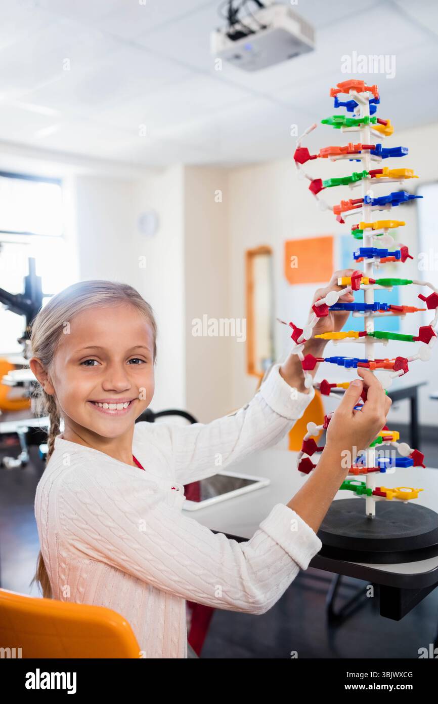 Mädchen, das buntes DNA-Helix-Modell im hellen Wissenschaftslabor in der Nähe des Fensters mit Tablette und Mikroskop zusammenbaut Stockfoto