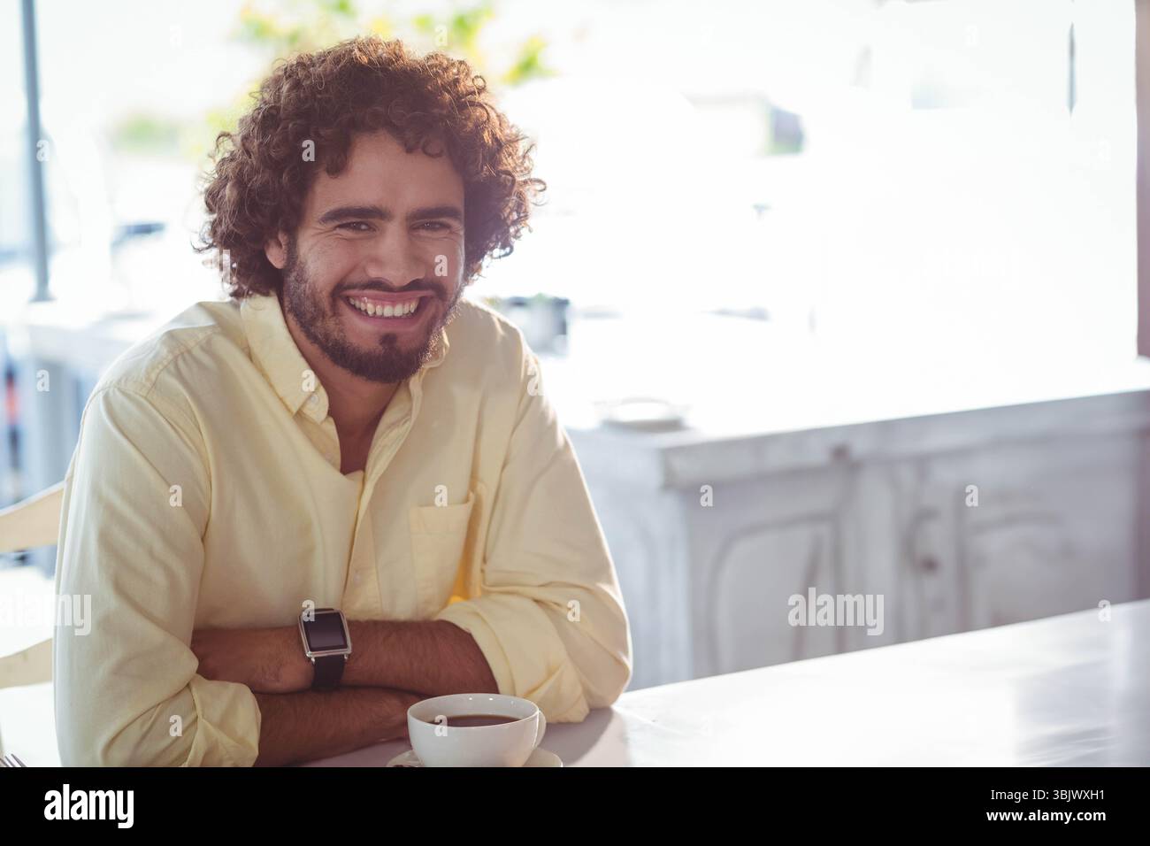 Mann Mitte Zwanziger mit gelbem Hemd, lächelt bei Kaffeetasse im Café, Kopierraum Stockfoto