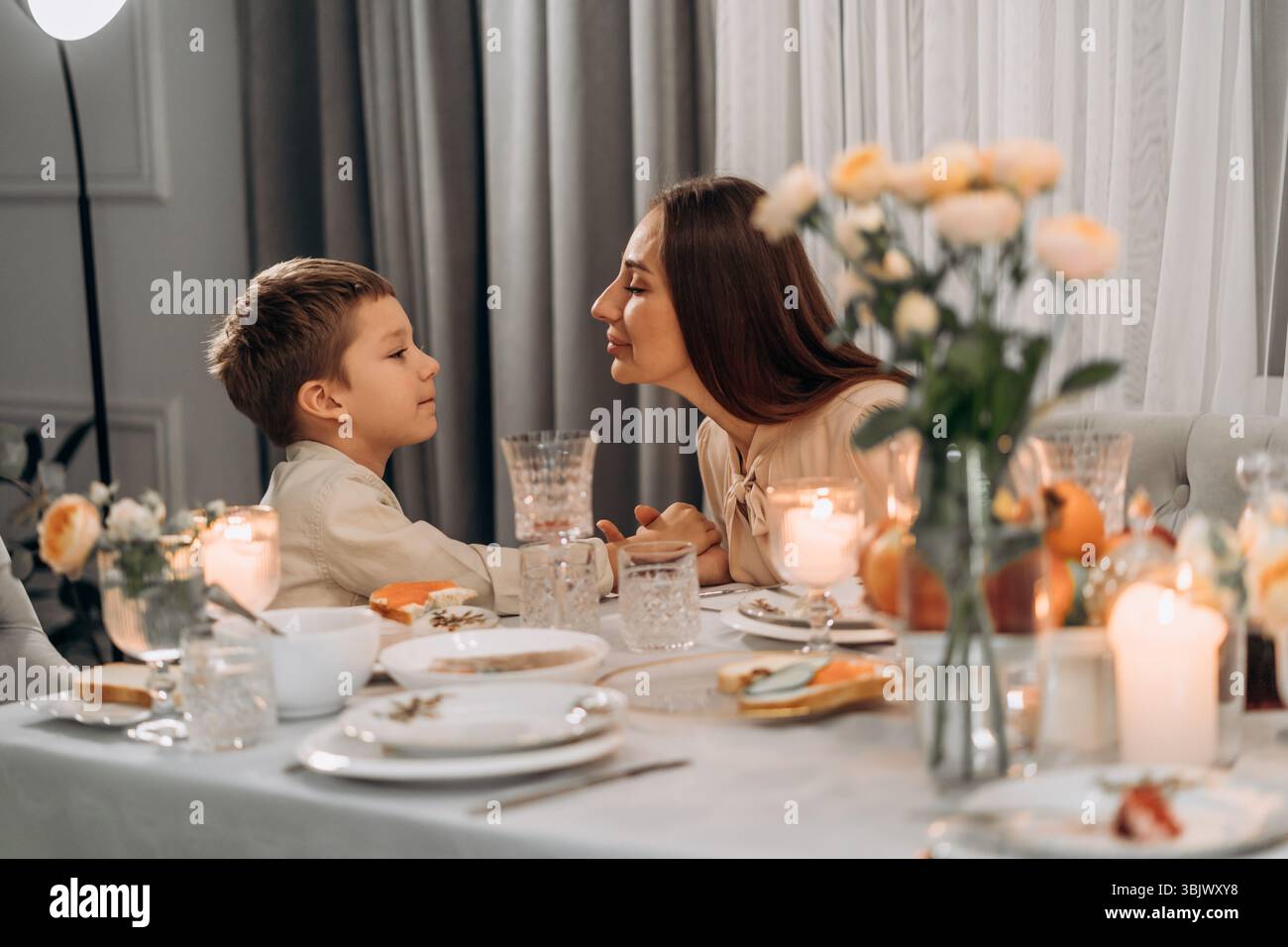 Zarte Nase-zu-Nase-Momente zwischen lächelnder Mutter und Sohn während des gemütlichen Abendessens, die Liebe, Wärme und emotionale Verbindung symbolisieren, perfekt für Stockfoto