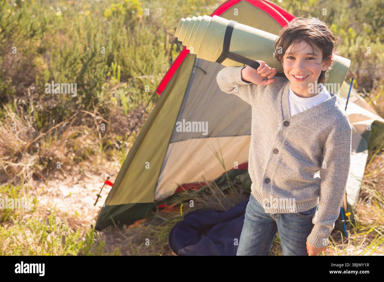 Junge mit grünem Schlafsofa neben rot getrimmtem Kuppelzelt auf Trockenfeld, Kopierraum Stockfoto