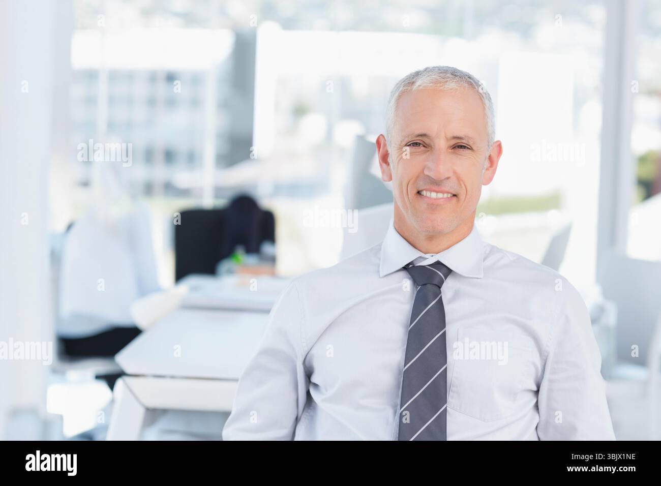 Älterer Mann mit Krawatte in einem ergonomischen Stuhl mit Laptop am Schreibtisch in der Nähe von Fenstern, Kopierraum Stockfoto
