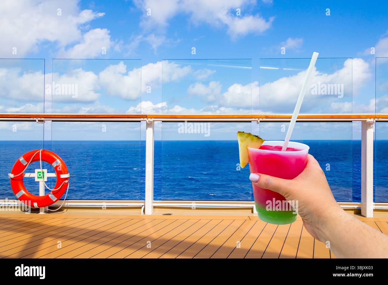 Hand hält ein Glas mit Cocktail und Stroh auf einem Deck des Kreuzfahrtschiffs mit Ozean auf dem Hintergrund mit Kopierraum Stockfoto