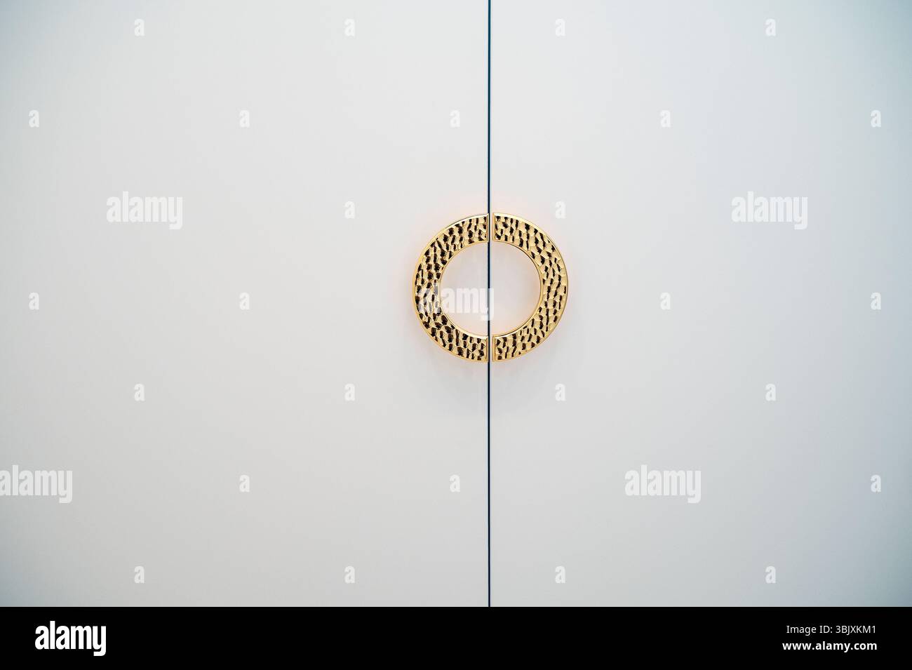 goldener runder Griff an weißen Schranktüren. Der Griff hat eine abgerundete Form, Stockfoto