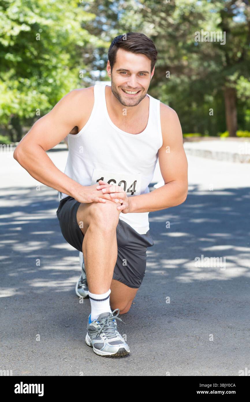 Männlicher Läufer kniend auf der Parkstraße mit Knie, lächelnd in Sportbekleidung mit Laufschuhen, Lätzchen 1604 Stockfoto