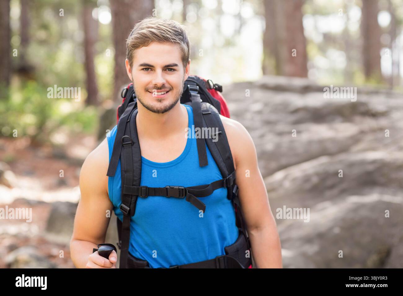 Mann, der auf bewaldetem Weg wandert, trägt ein blaues Tanktop mit einem Trekkingstock und trägt einen Rucksack Stockfoto