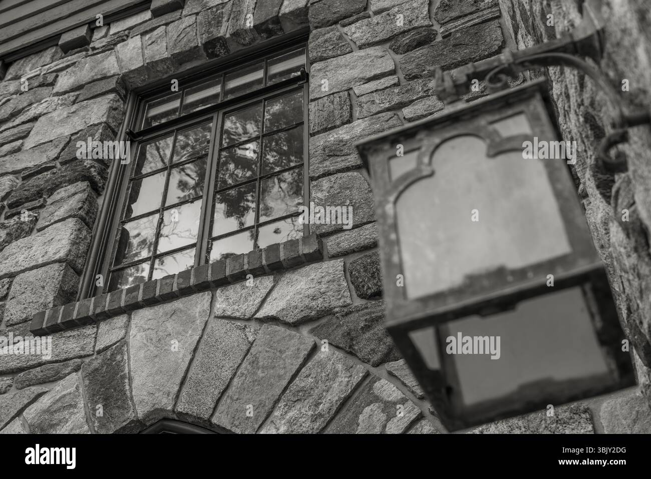 Schwarz-weiß-Foto von Steinmauer, altes Fenster mit Reflexionen, Vintage-Metall-Laterne, rustikale Textur, historisches Gebäudedetail. Stockfoto