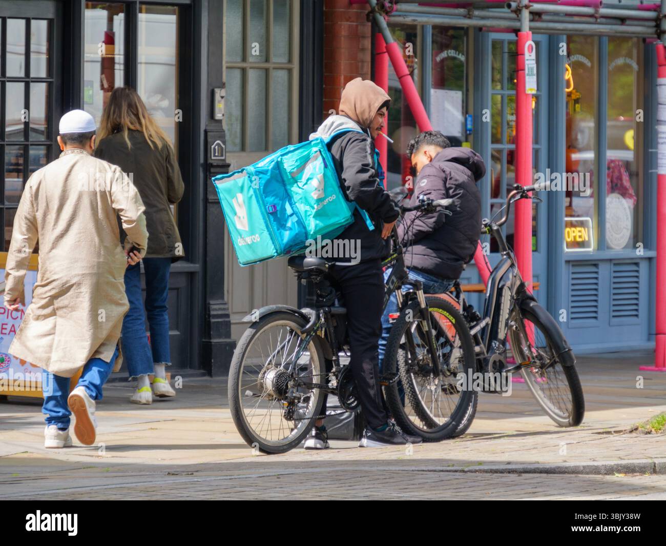 Ein Deliveroo-Fahrer macht eine Zigarettenpause in Spitalfields, London, Großbritannien, und bietet einen offenen Einblick in die Ausfallzeiten der Arbeiter in der Gig Economy in der Stadt Stockfoto
