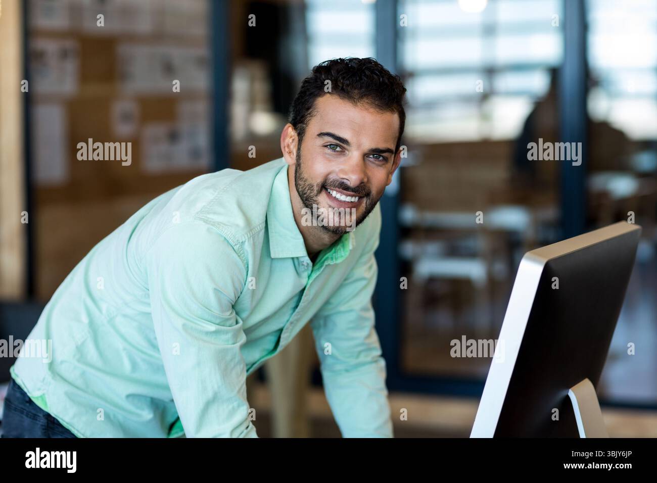 Desktop-Computer-Monitor mit Datenanzeige auf dem Schreibtisch in einem modernen Büro mit hölzernem Pinnwand hinten Stockfoto