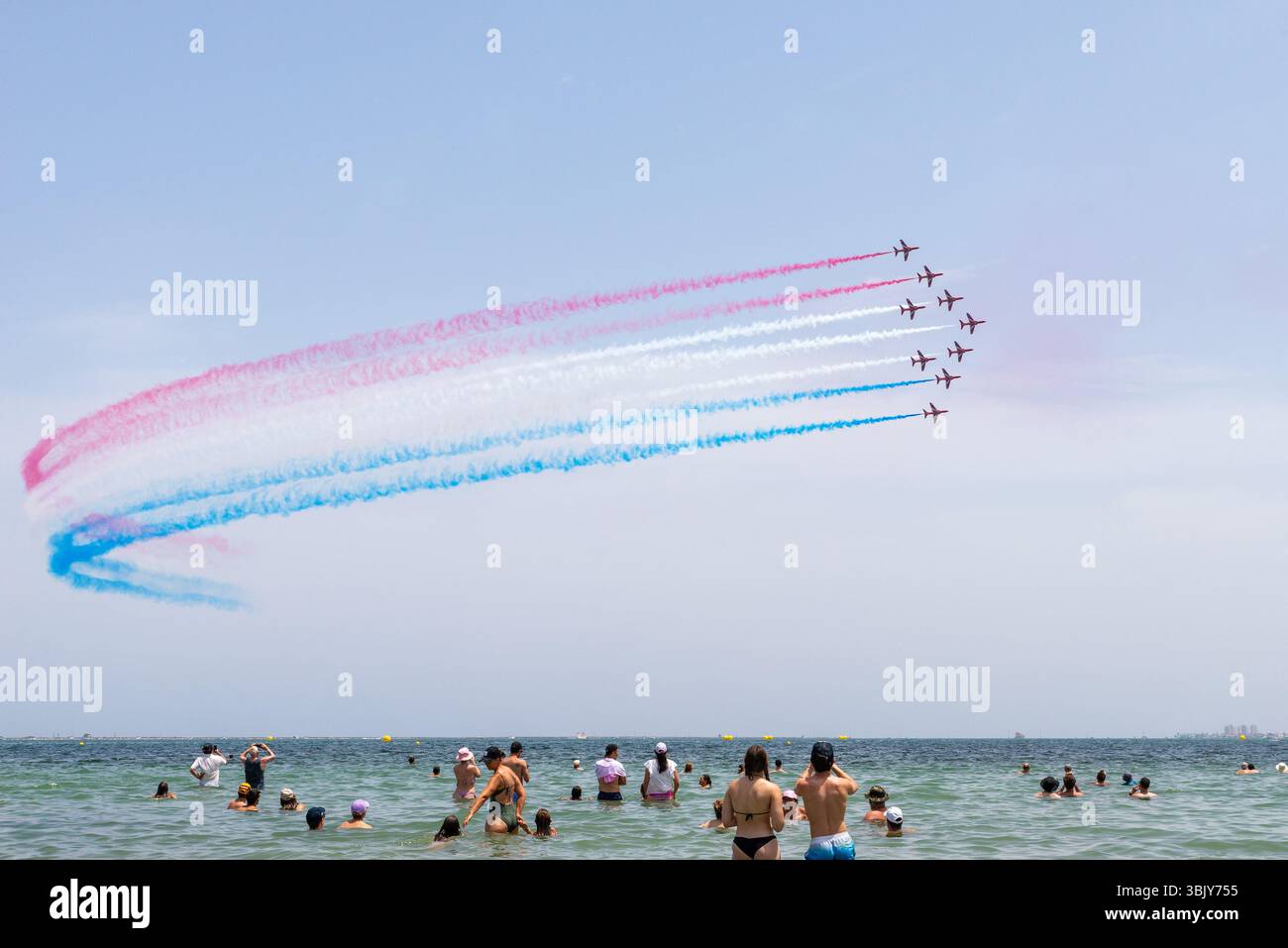 Rote Pfeile der Royal Air Force zeigen ein Team, das über den Mar Menor mit rot-weiß-blauem Rauchpfad fliegt. San Javier AIRE25 Airshow. Menschenmassen im Mittelmeer Stockfoto
