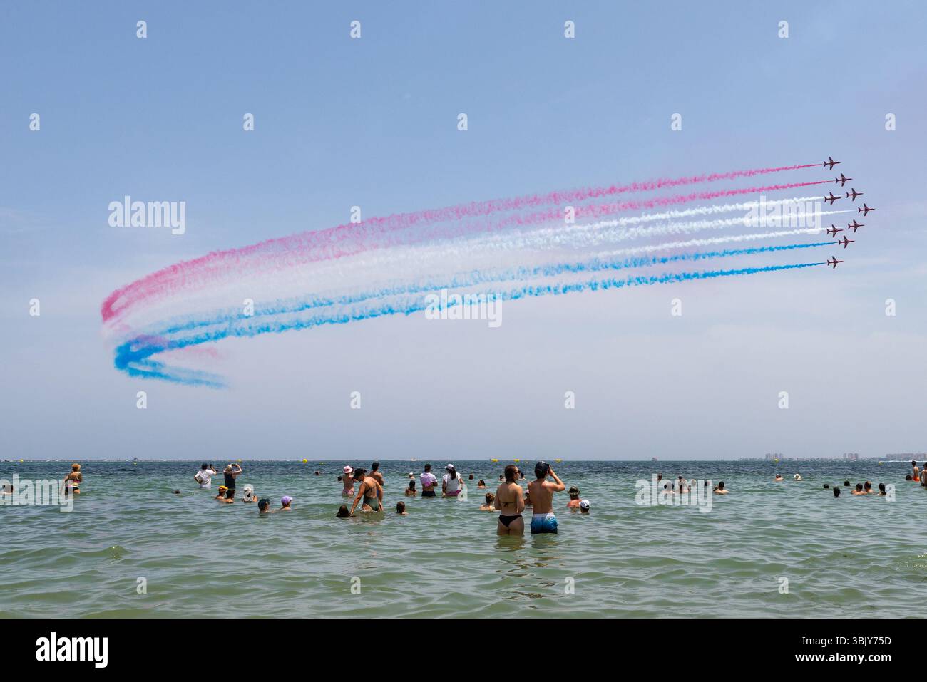 Rote Pfeile der Royal Air Force zeigen ein Team, das über den Mar Menor mit rot-weiß-blauem Rauchpfad fliegt. San Javier AIRE25 Airshow. Menschenmassen im Mittelmeer Stockfoto