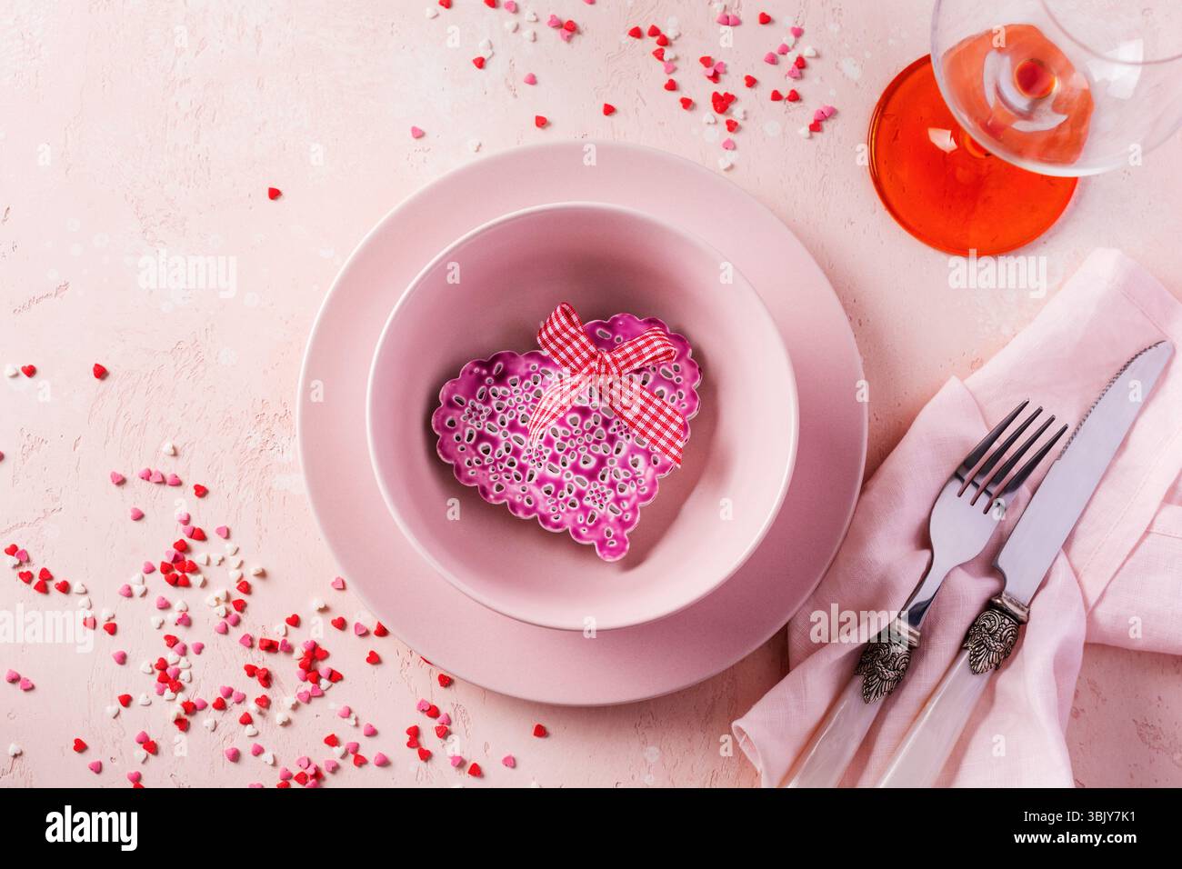 Valentinstag Tischeinstellung mit rosafarbenem Teller und Geschenkherz auf rosa hellem Hintergrund Stockfoto