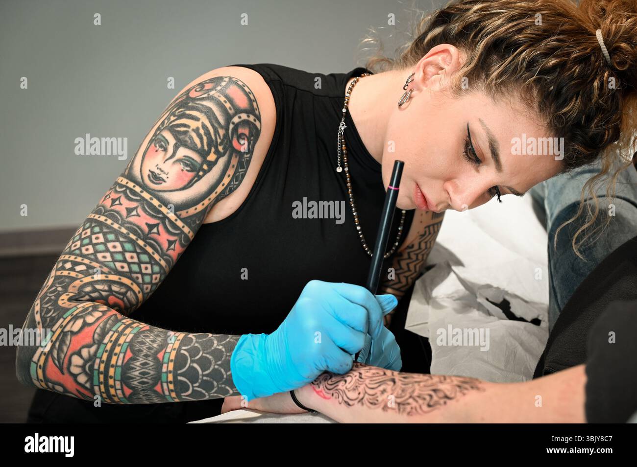 Der Tätowierer zeichnet sorgfältig schwarze Linien auf den Arm eines Kunden, um ein wunderschönes Stück Körperkunst zu kreieren Stockfoto