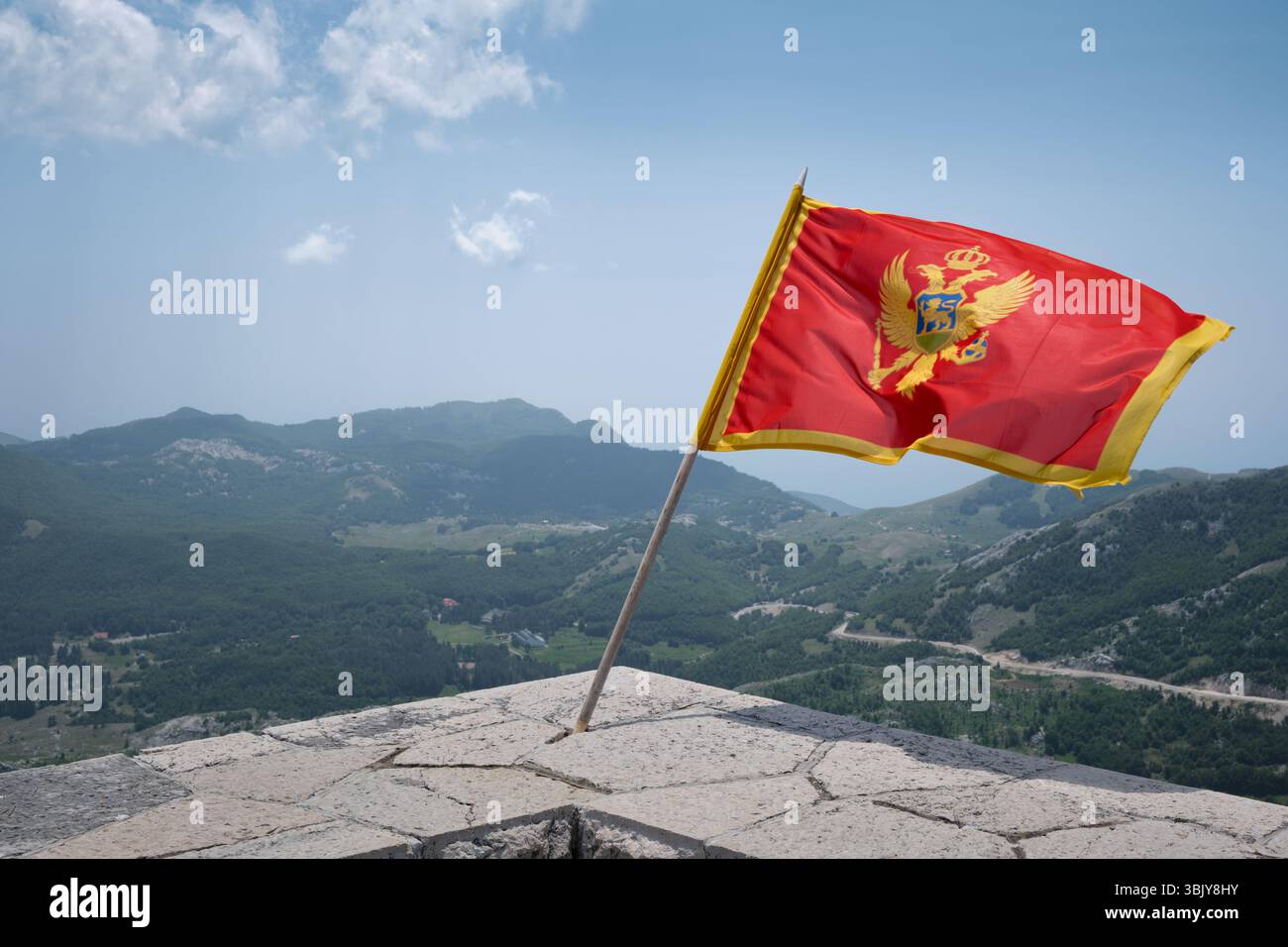 Lovćen, Montenegro – 13. Juni 2025: Nationalflagge Montenegros winkt im Wind auf einem Aussichtspunkt in den Bergen im Nationalpark Lovćen. Stockfoto