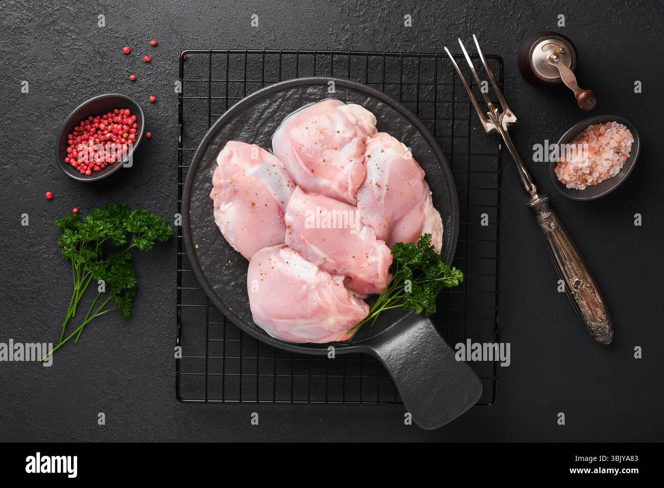 Rohes Hähnchenschenkelfilet ohne Haut mit Kräutern und Gewürzen auf schwarzem Hintergrund. Fleisch von Geflügel in landwirtschaftlichen Betrieben. Draufsicht mit Kopierbereich. Mo Stockfoto