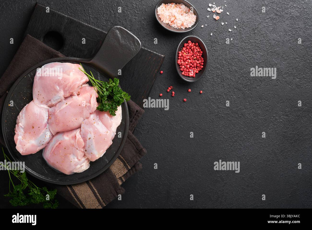 Rohes Hähnchenschenkelfilet ohne Haut mit Kräutern und Gewürzen auf schwarzem Hintergrund. Fleisch von Geflügel in landwirtschaftlichen Betrieben. Draufsicht mit Kopierbereich. Mo Stockfoto
