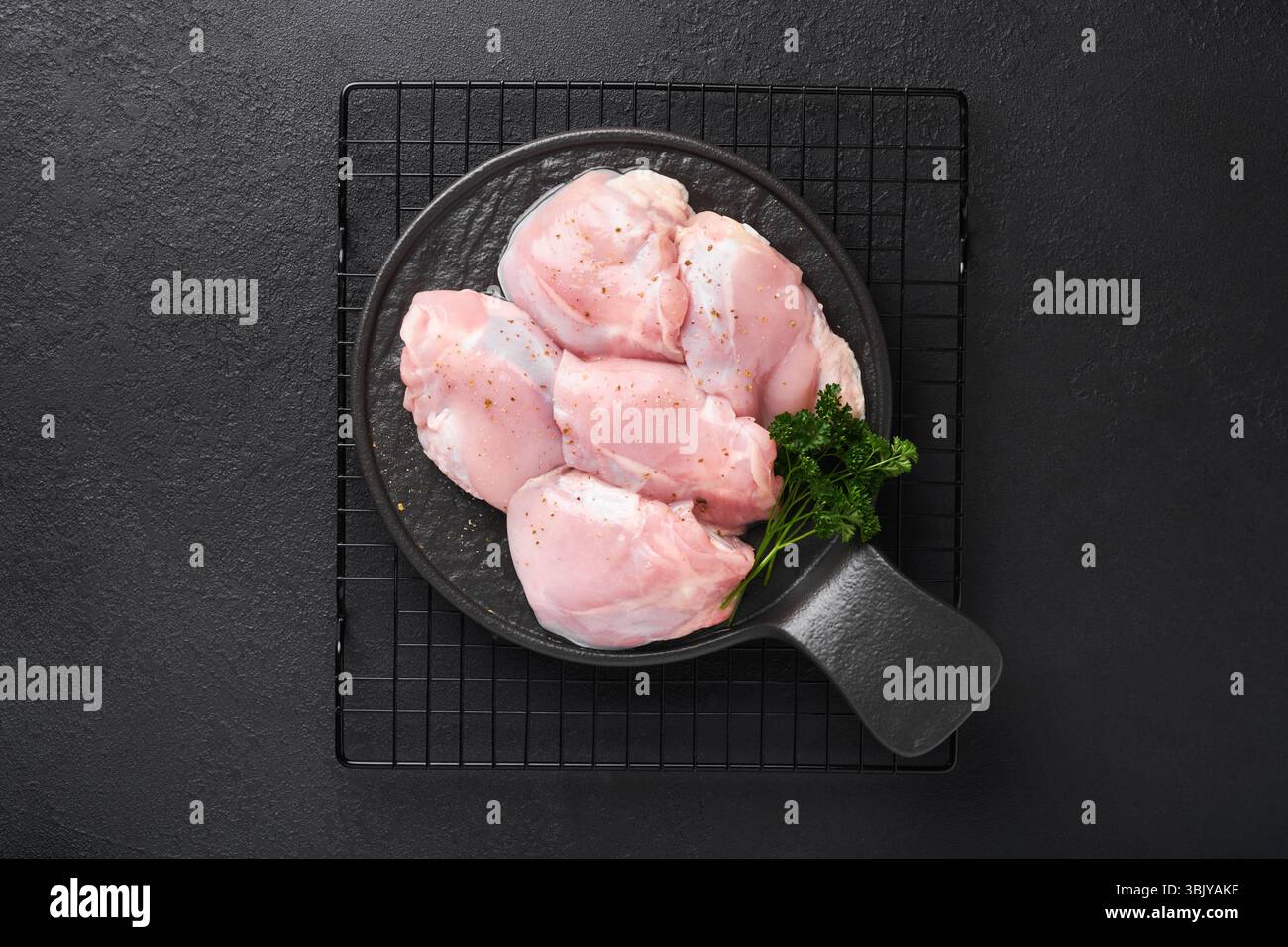 Rohes Hähnchenschenkelfilet ohne Haut mit Kräutern und Gewürzen auf schwarzem Hintergrund. Fleisch von Geflügel in landwirtschaftlichen Betrieben. Draufsicht mit Kopierbereich. Mo Stockfoto