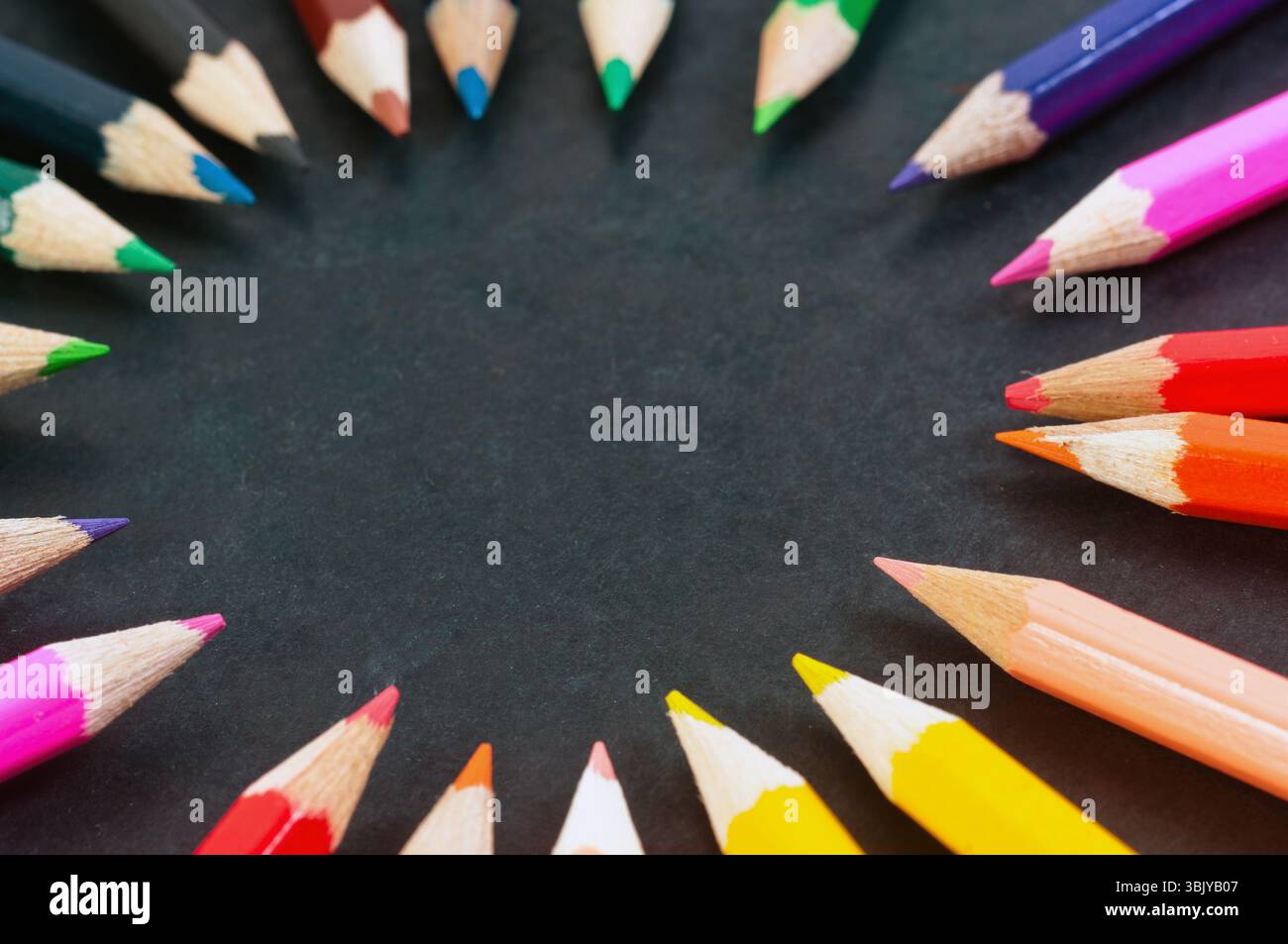 Bunte Bleistifte auf dunklem Hintergrund im Kreis Stockfoto