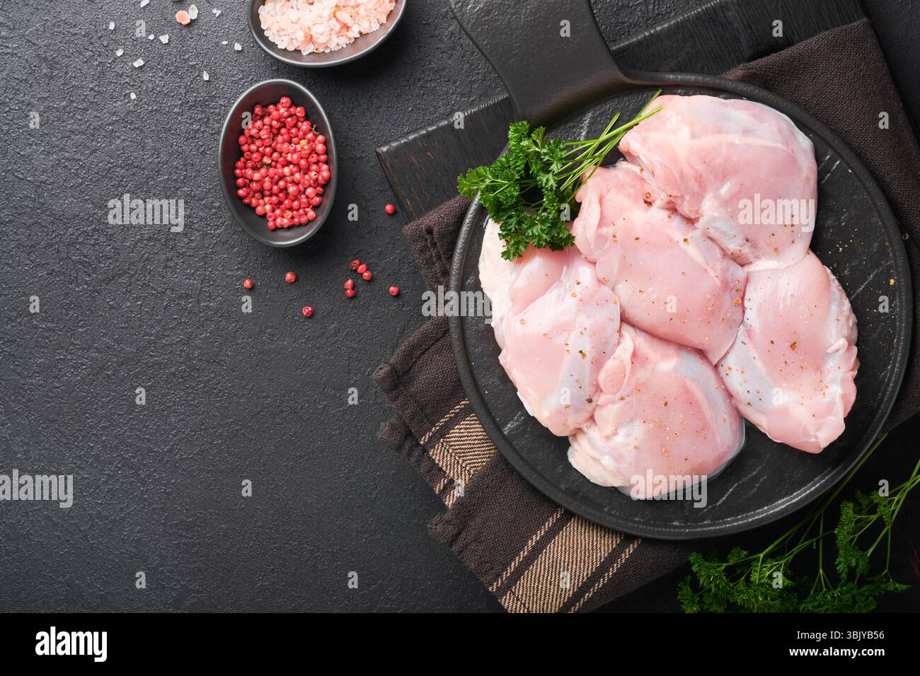 Rohes Hähnchenschenkelfilet ohne Haut mit Kräutern und Gewürzen auf schwarzem Hintergrund. Fleisch von Geflügel in landwirtschaftlichen Betrieben. Draufsicht mit Kopierbereich. Mo Stockfoto