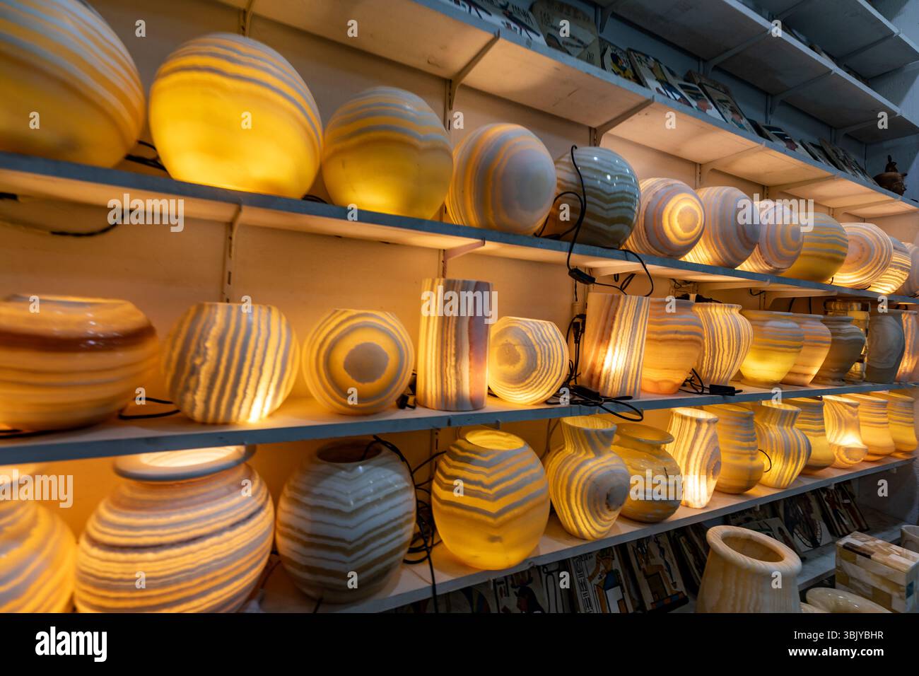 In den Regalen finden Sie eine Sammlung beleuchteter, gestreifter Alabaster-Lampen in verschiedenen Formen, darunter Kugeln, Zylinder und Vasen, die ihren warmen Glanz und ihre dekorative Wirkung zum Ausdruck bringen. Stockfoto