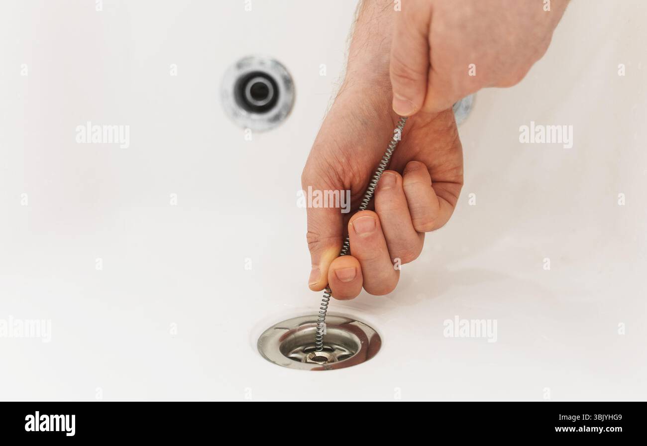 Klempner, der die Badewanne mit einer Abflussschlange entklumpt hat. Stockfoto