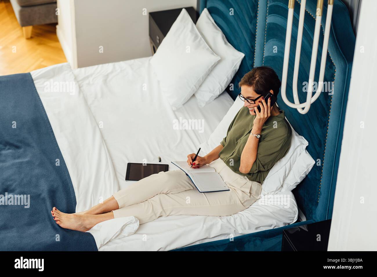 High-Angle-Ansicht der Frau in formelle Kleidung liegend auf Das Bett sprach über ein Mobiltelefon mit einem Notebook auf ihr Hüften Stockfoto
