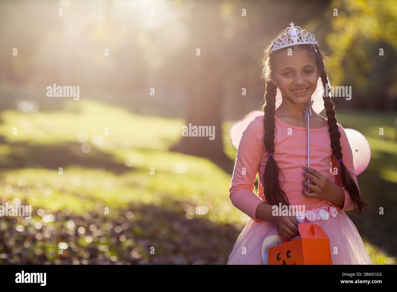 Kürbis-förmige Trick-or-Treat-Tasche, die auf einem grasbewachsenen Feld unter sonnendurchfluteten Bäumen mit Blattstreuung sitzt Stockfoto