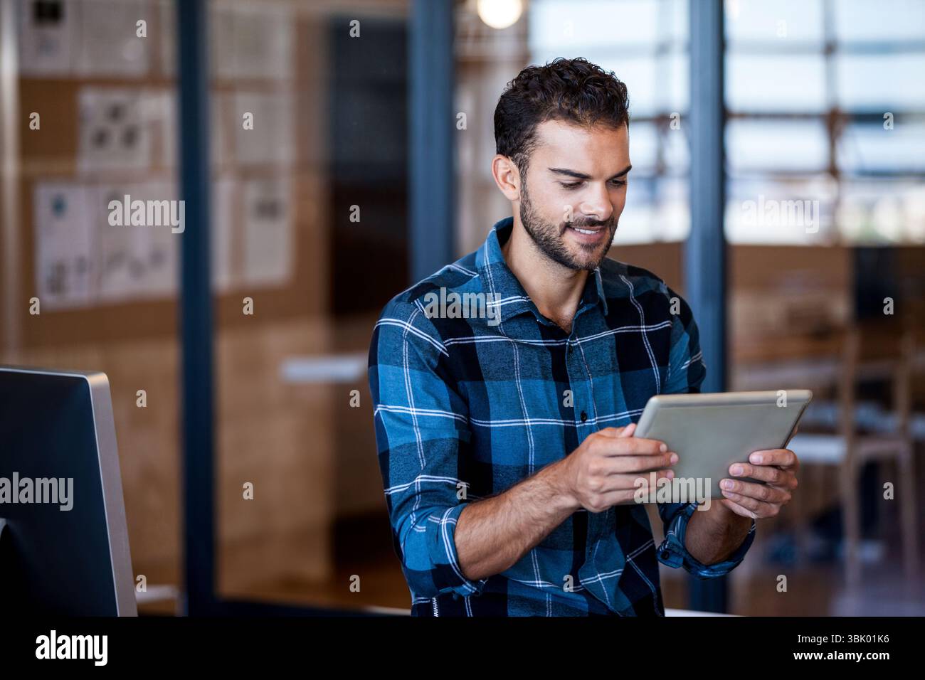 Monitor, der auf dem Schreibtisch hinter einer Glaswand leuchtet, zeigt Korkbrett mit festgehefteten Papieren Stockfoto