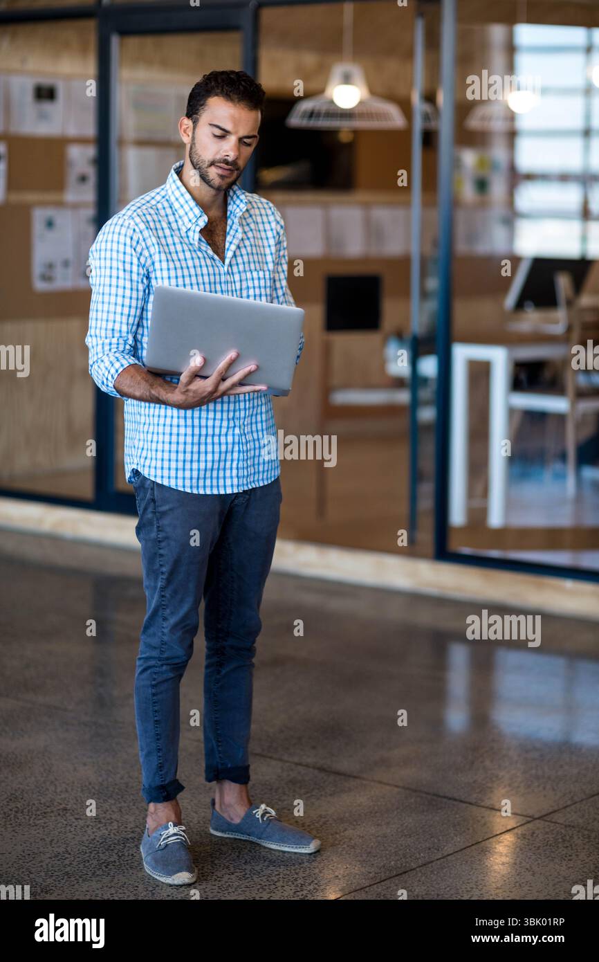 Silberner Laptop auf weißem Schreibtisch in der modernen Bürolobby mit Glasabtrennungen und gesteppten Papieren Stockfoto