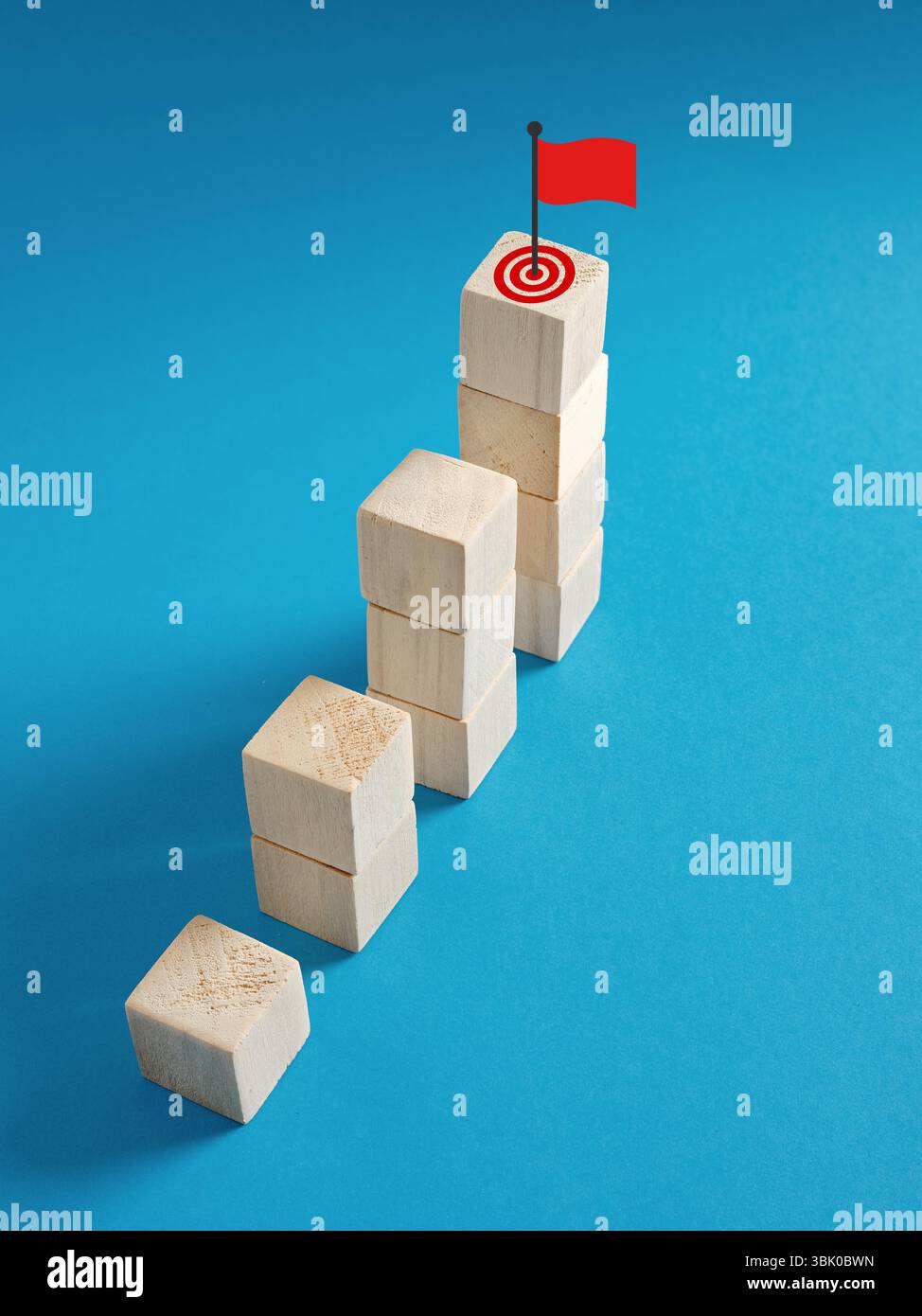 Konzept von Wachstum, Fortschritt und Zielerreichung symbolisiert durch aufsteigende Holzblöcke mit Ziel und roter Flagge. Stockfoto