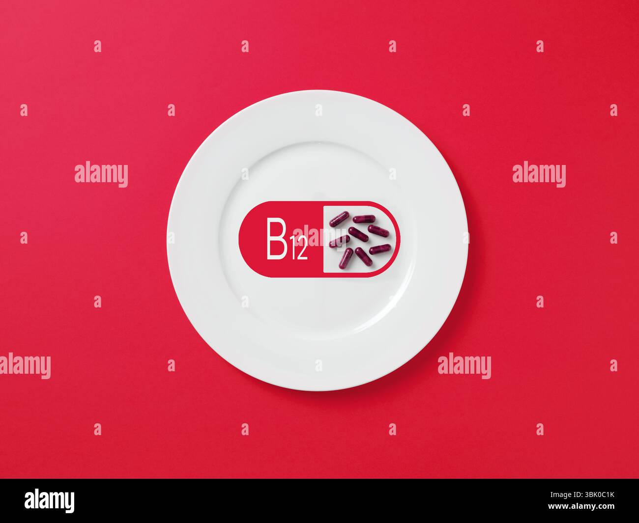 Weiße Platte mit einem b12-Symbol und Pillen auf rotem Hintergrund, die die Bedeutung von Vitaminen für eine ausgewogene Ernährung symbolisieren Stockfoto