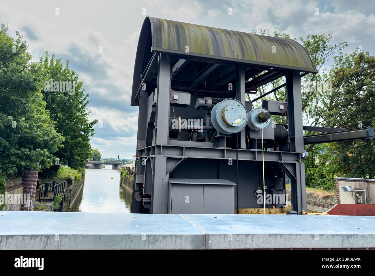 Eine große historische Wasserstraße steht neben einem ruhigen Kanal und zeigt komplizierte Maschinen. Üppiges Grün umgibt die Szene mit einem bewölkten Himmel o Stockfoto