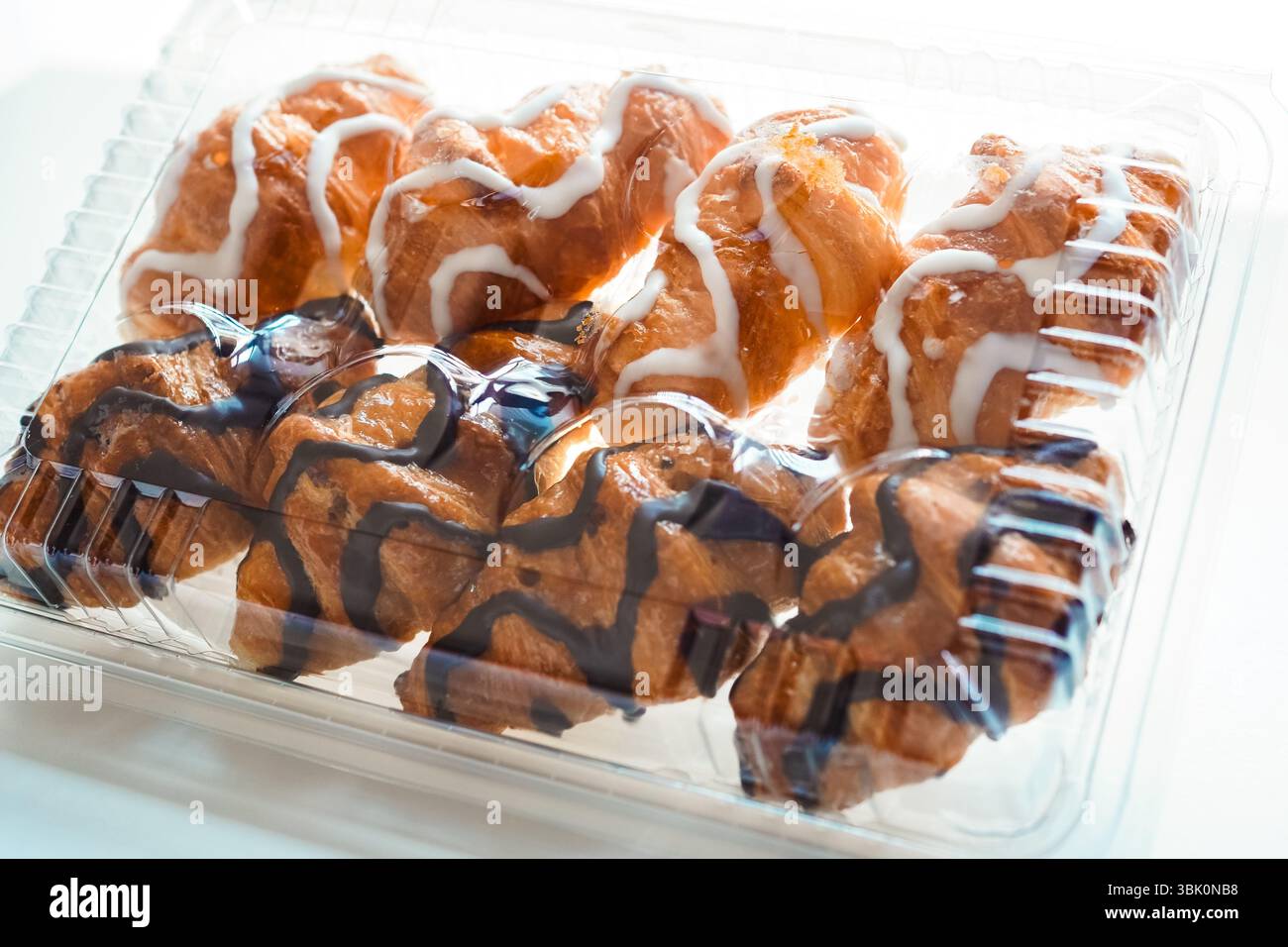 Mini-Croissants aus weißer und schwarzer Schokolade, die in Kunststoff-Croissant-Behältern auf weißem Hintergrund verkauft werden Stockfoto