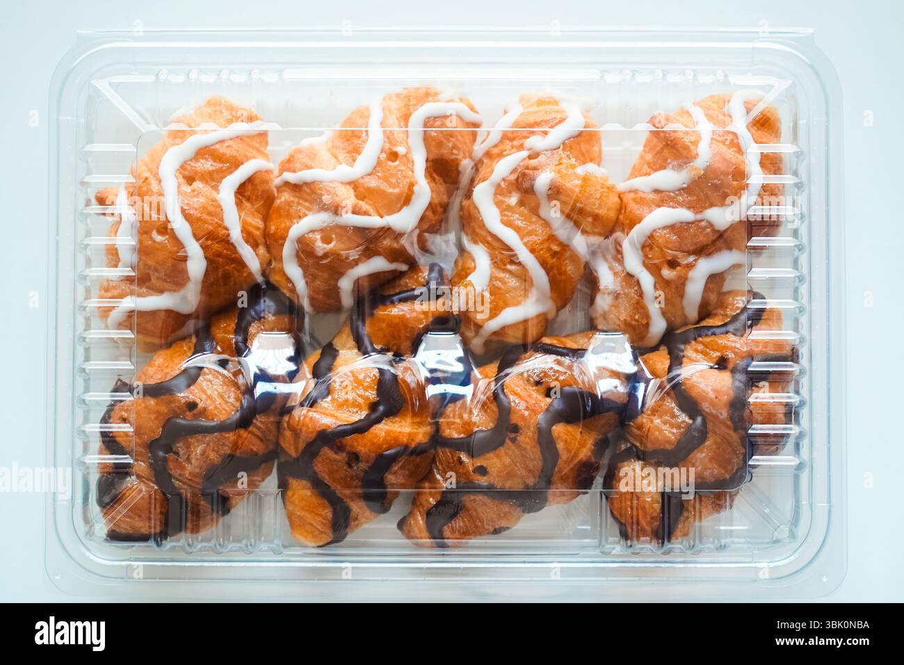 Mini-Croissants aus weißer und schwarzer Schokolade, die in Kunststoff-Croissant-Behältern auf weißem Hintergrund verkauft werden Stockfoto