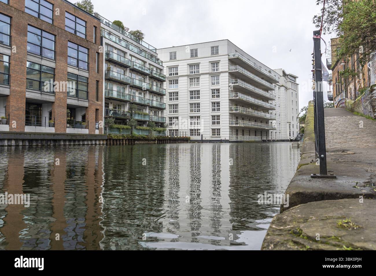 Moderne und historische Gebäude spiegeln sich an einem bewölkten Tag im ruhigen Wasser des Regent's Canal in der Stadt london wider Stockfoto