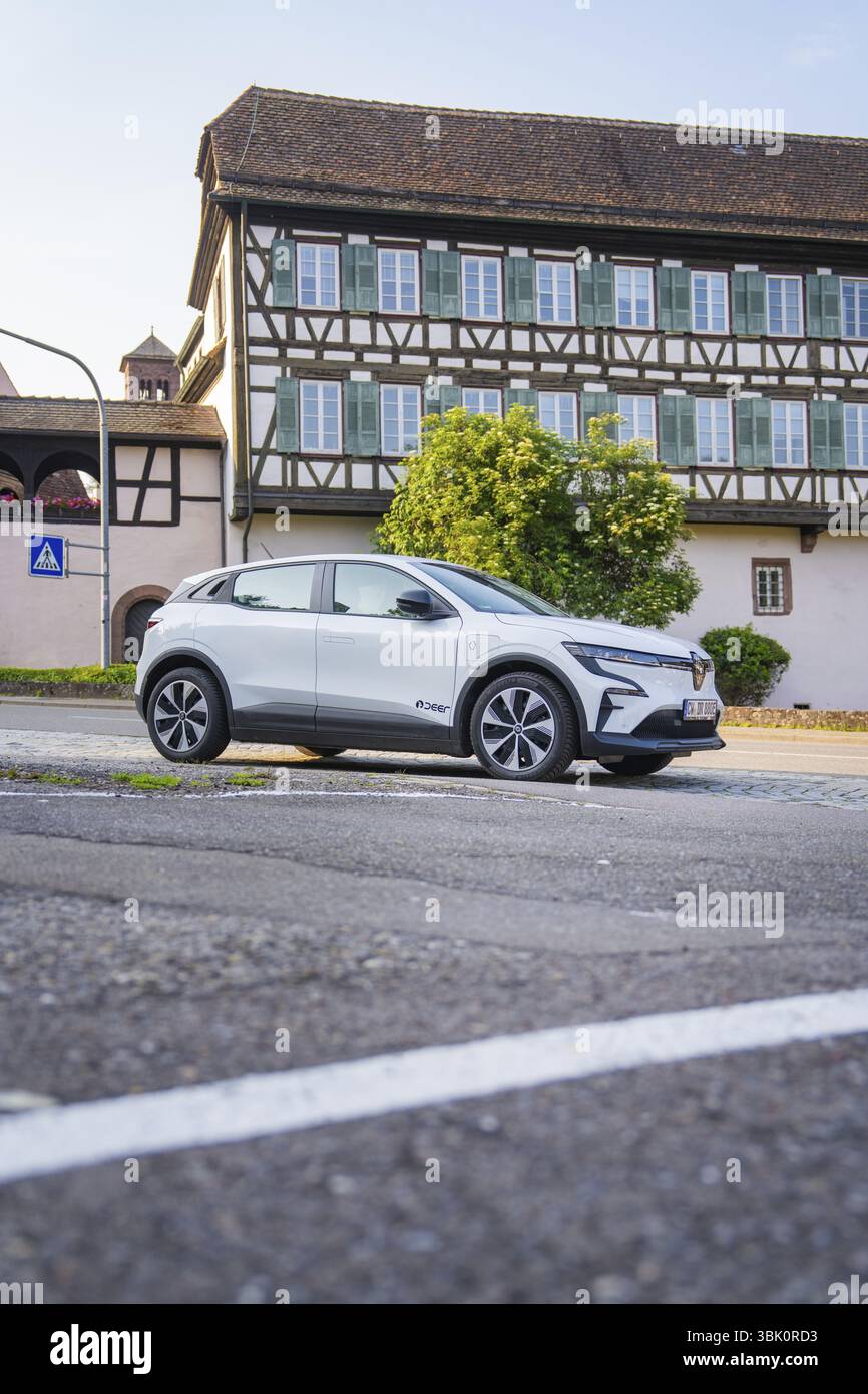 Weißes Auto parkt auf einer städtischen Straße vor einem großen, traditionellen Fachwerkhaus im Sommer, Renault Megane, Deer E Carsharing, Elektroauto C Stockfoto