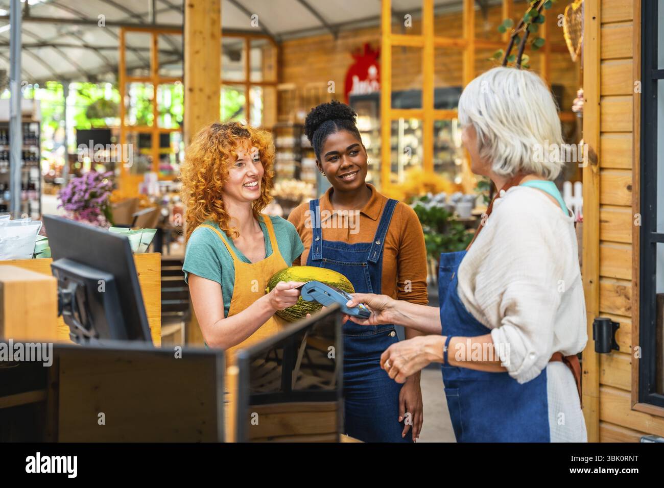 Kunde, der mit kontaktloser Zahlung in einem Lebensmittelgeschäft bezahlt, unterstützt von zwei lächelnden Ladenassistenten Stockfoto