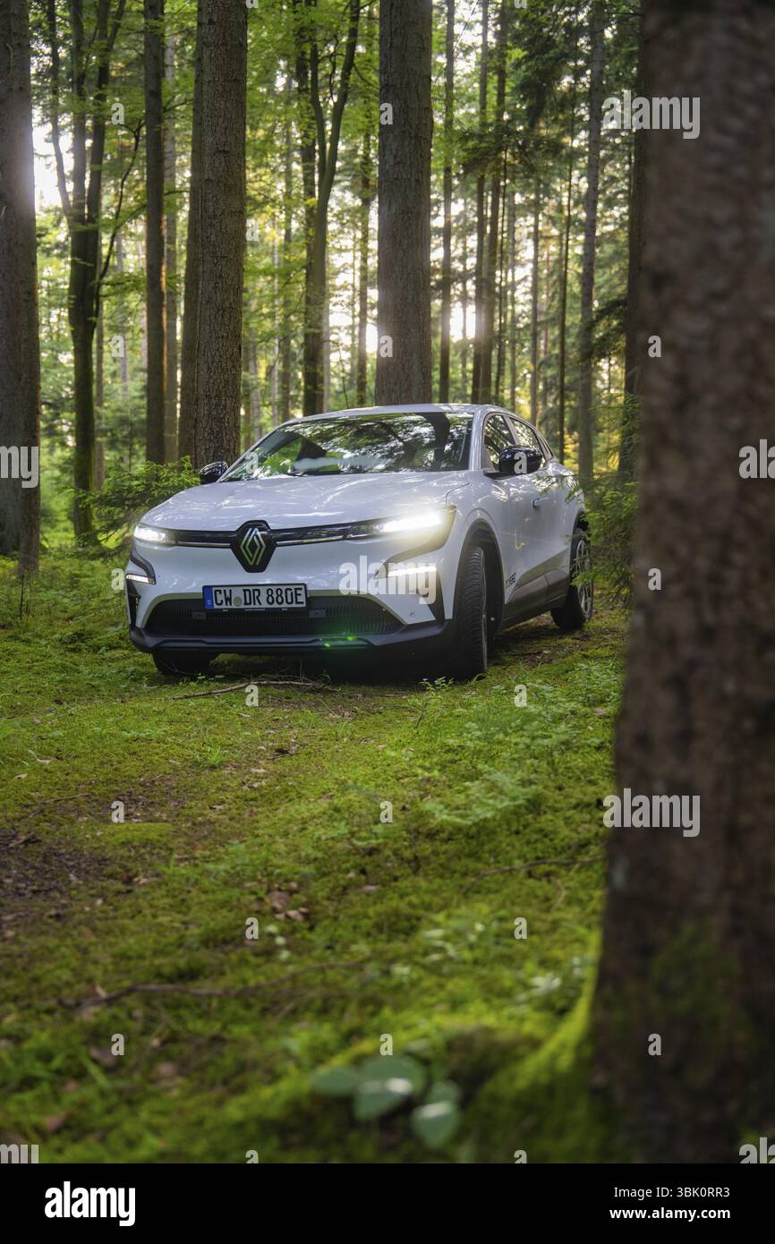 Weißes Auto, das durch einen hellen Wald mit Sonnenstrahlen zwischen den Bäumen fährt, Renault Megane, Deer E Carsharing, Elektroauto, Calw, Schwarzwald, Deutschland Stockfoto