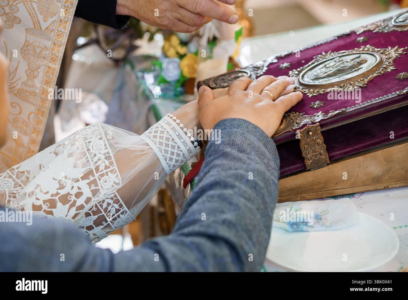 Nahaufnahme einer Hochzeitszeremonie mit Händen über einem reich verzierten religiösen Buch. spitzenärmel versprechen und lieben. Goldene Akzente, intim, tra Stockfoto